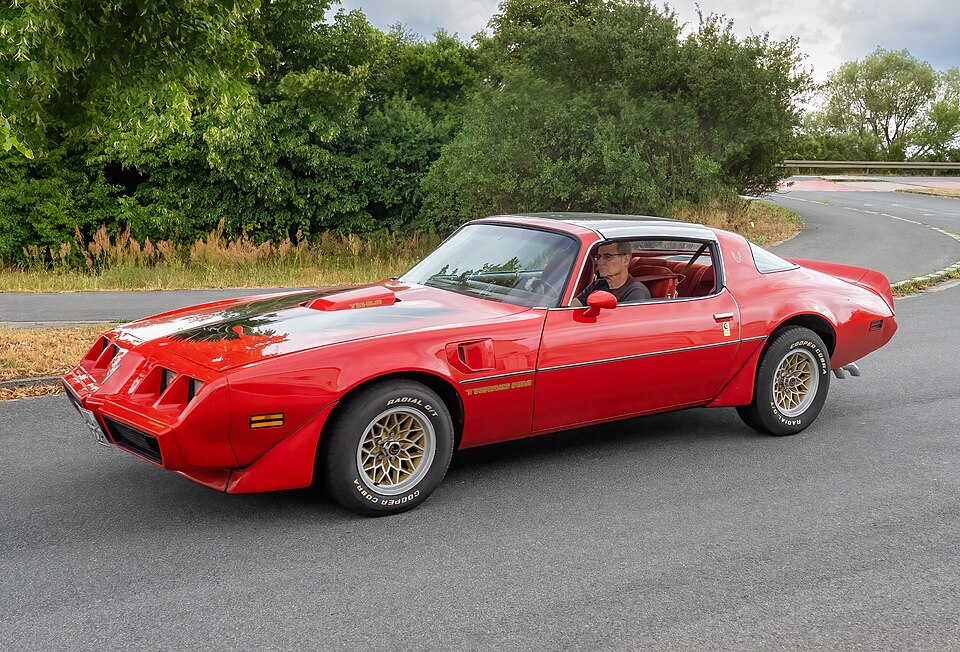 Red second-generation Pontiac Trans Am driving on a rural road